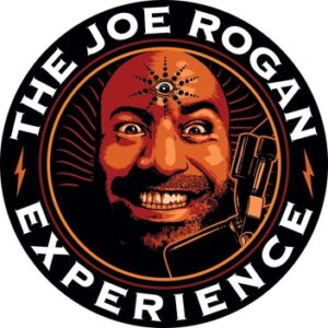 The cover art for The Joe Rogan Experience. A circular black and sepia toned logo with the title in white, all-caps serif font around the outside of the logo, and Rogan's grinning face in the middle. Rogan seems to have a third eye with decorative symbols around it on his forehead. A microphone is suspended in front of his face.